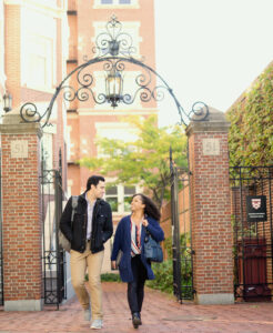 Dos estudiantes caminando bajo la puerta del campus de Harvard