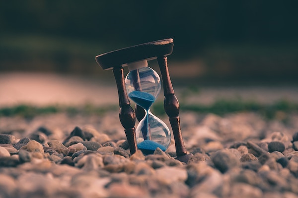 An hourglass with blue sand counts down time on a pebbly road.