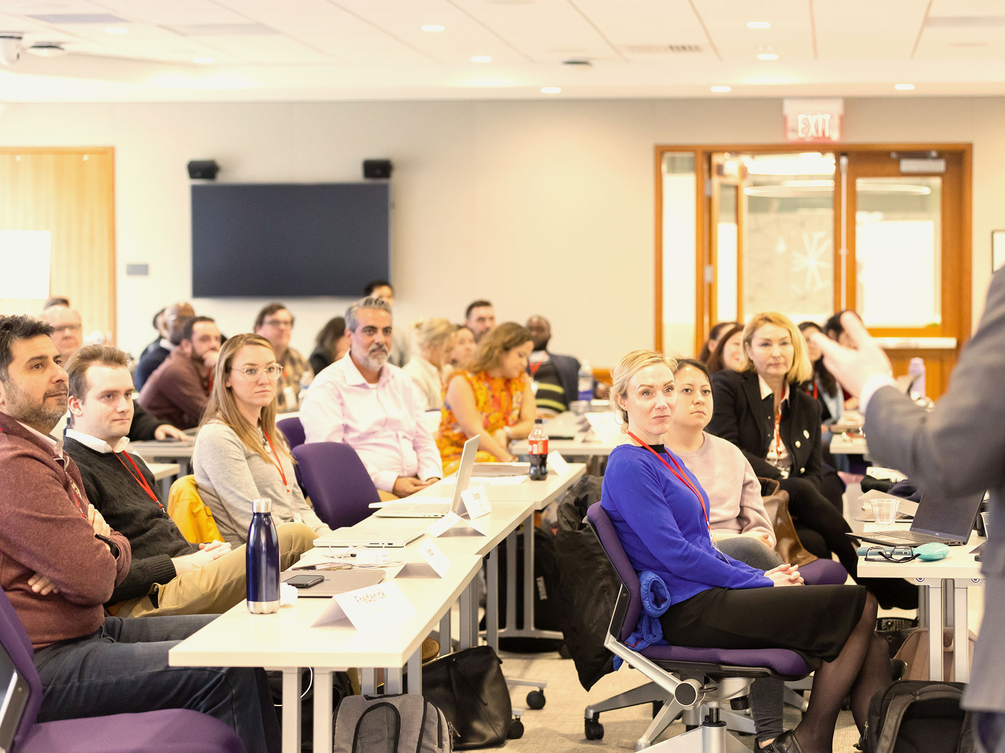 Group of adult learners seated in a classroom, listening to a speaker at the front.