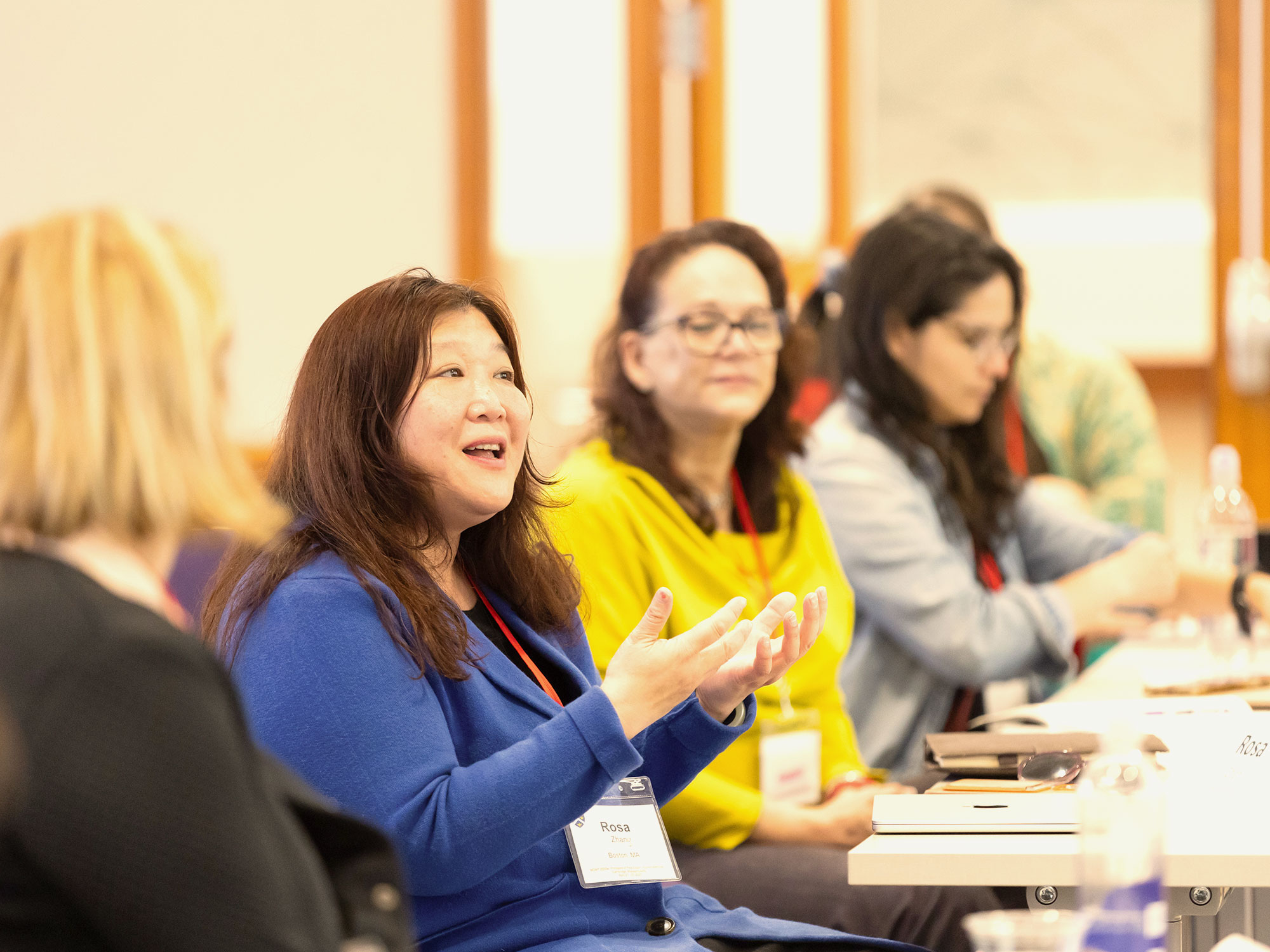 A woman in a blue sweater speaks while gesturing with her hands during a classroom discussion.