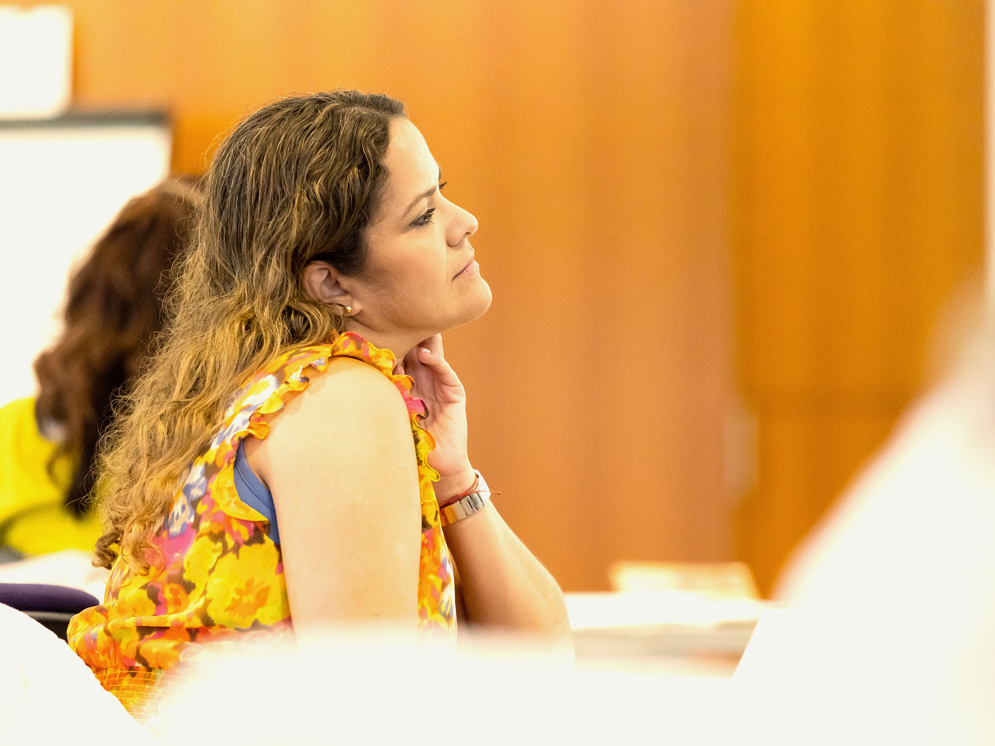 A woman in a floral top leans slightly forward, listening intently during a class.