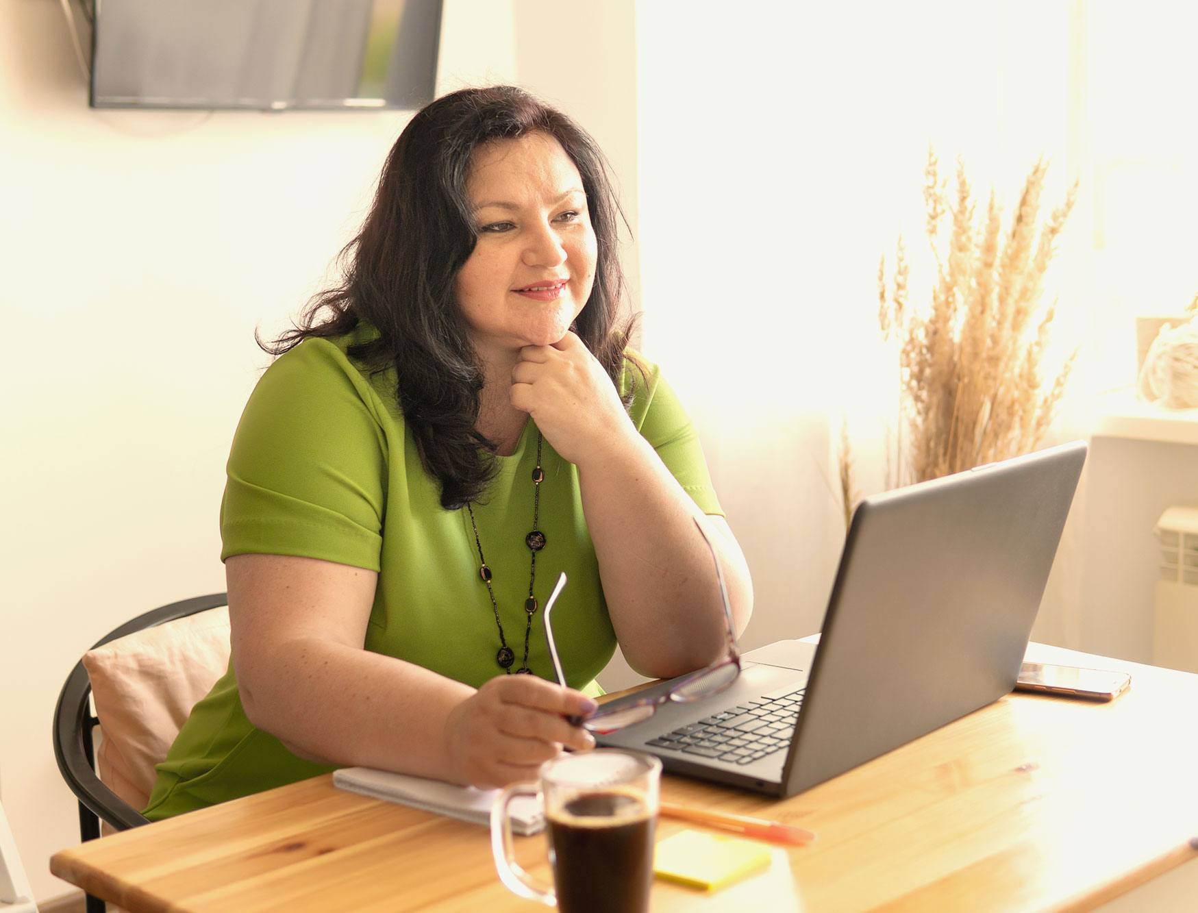 A woman sits in front of a laptop, looking thoughtful.
