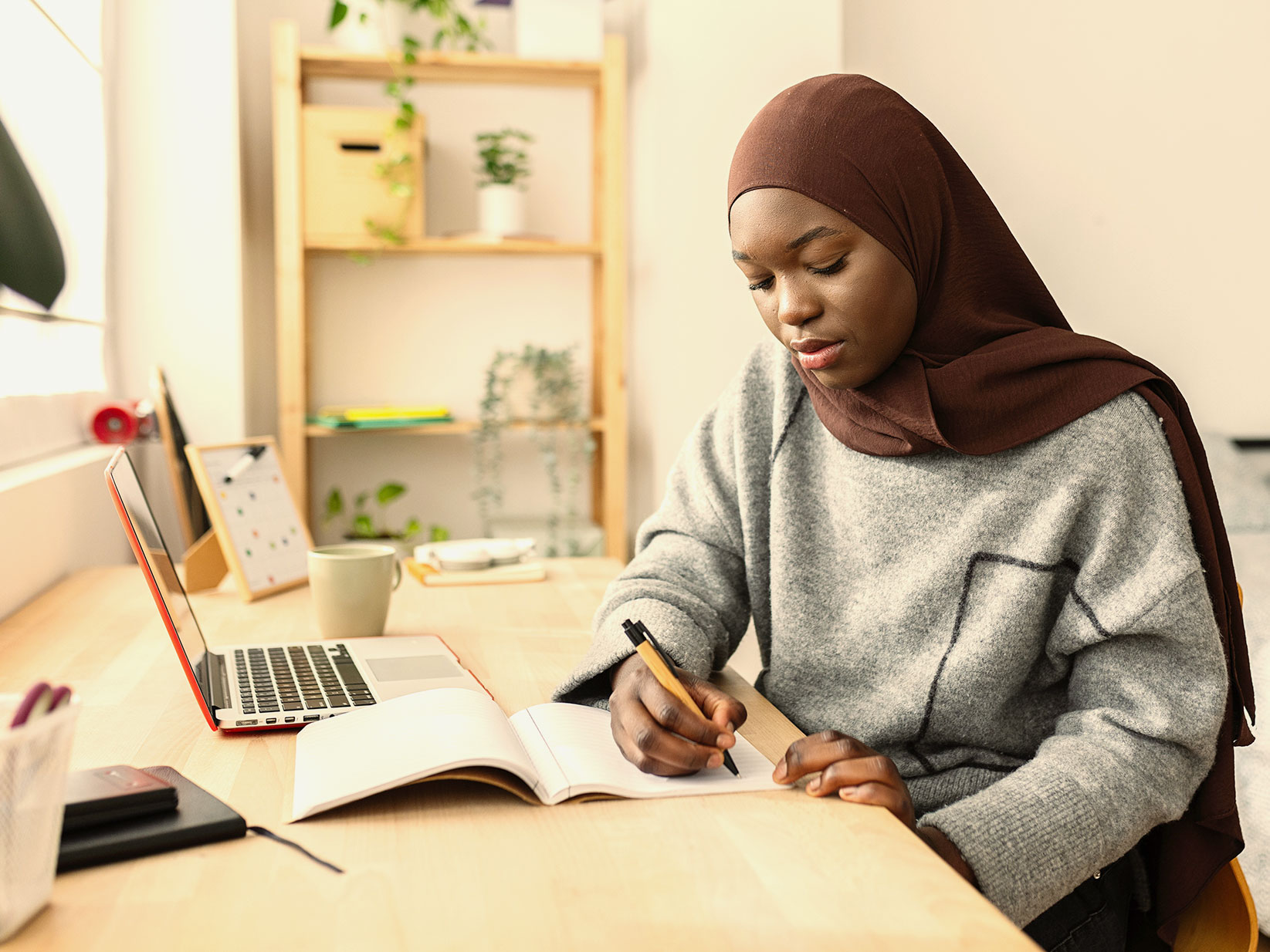 A woman wearing a hijab sits at a desk doing homework.
