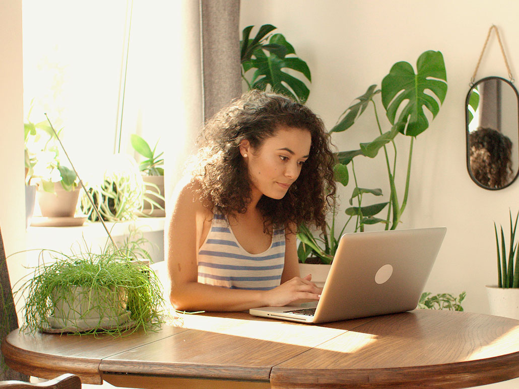 A woman sits at a laptop at a dining table.