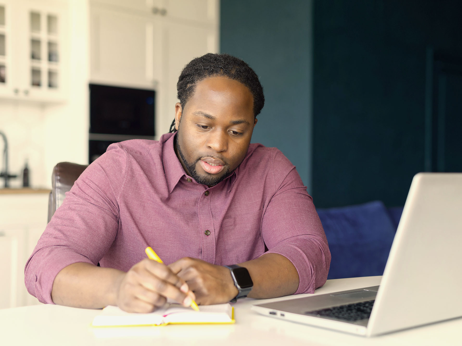 A man takes notes in front of a laptop.