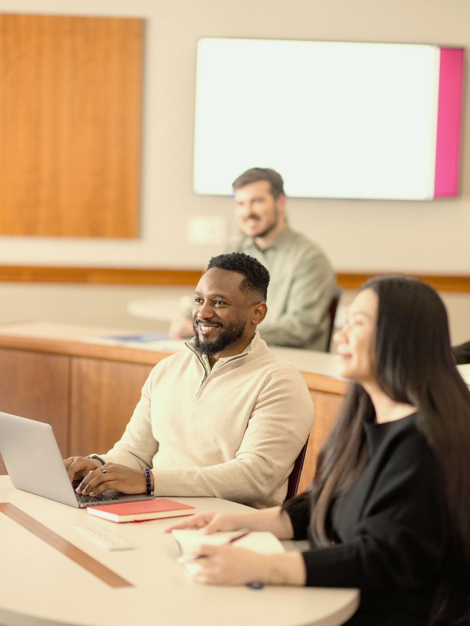 Three students sit in a classroom, listening to an instructor speak out of frame.