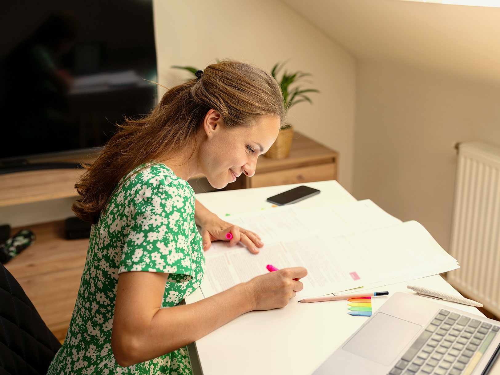 A woman highlights documents next to an open laptop.