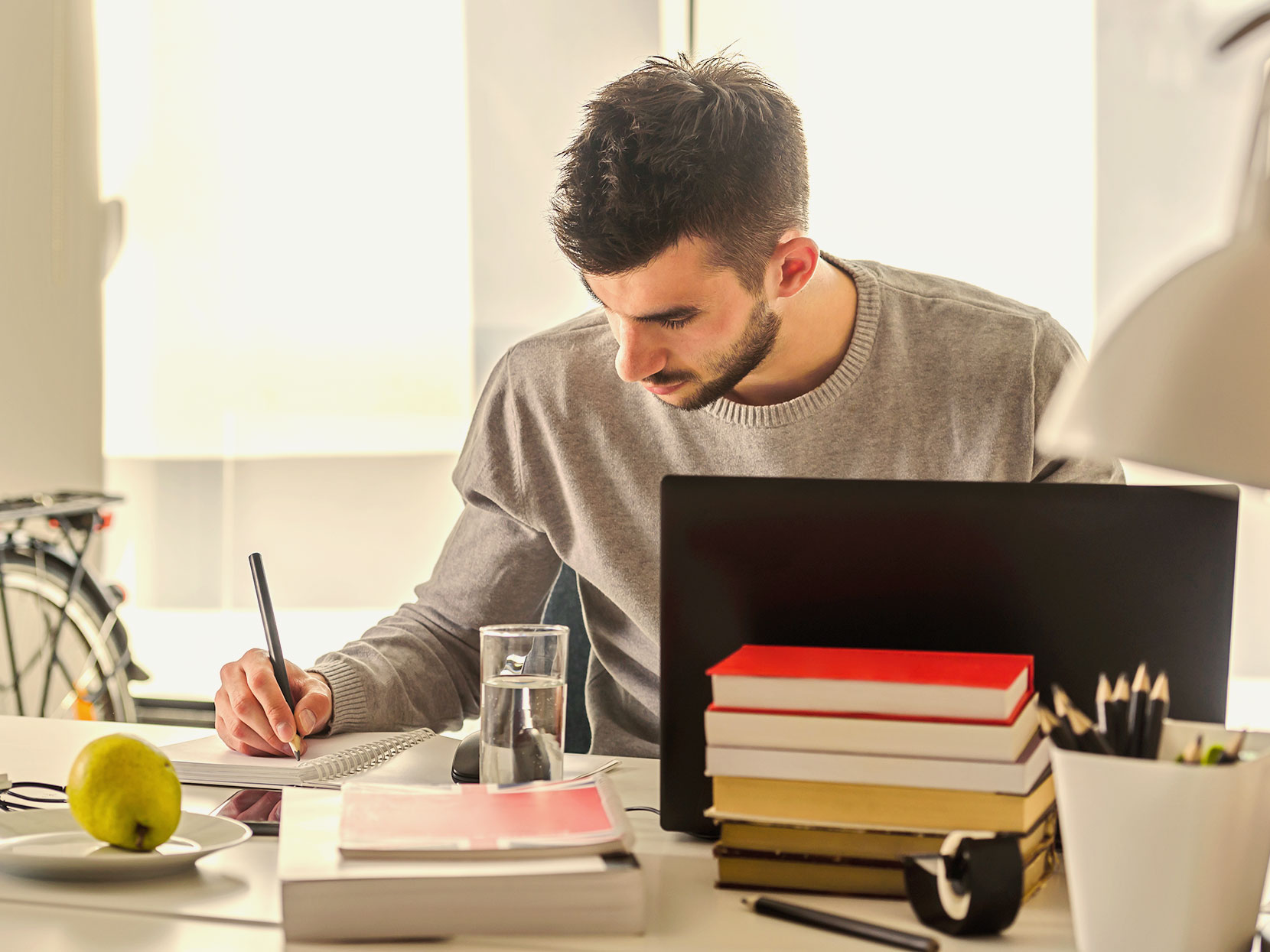 A man takes notes in front of a laptop.