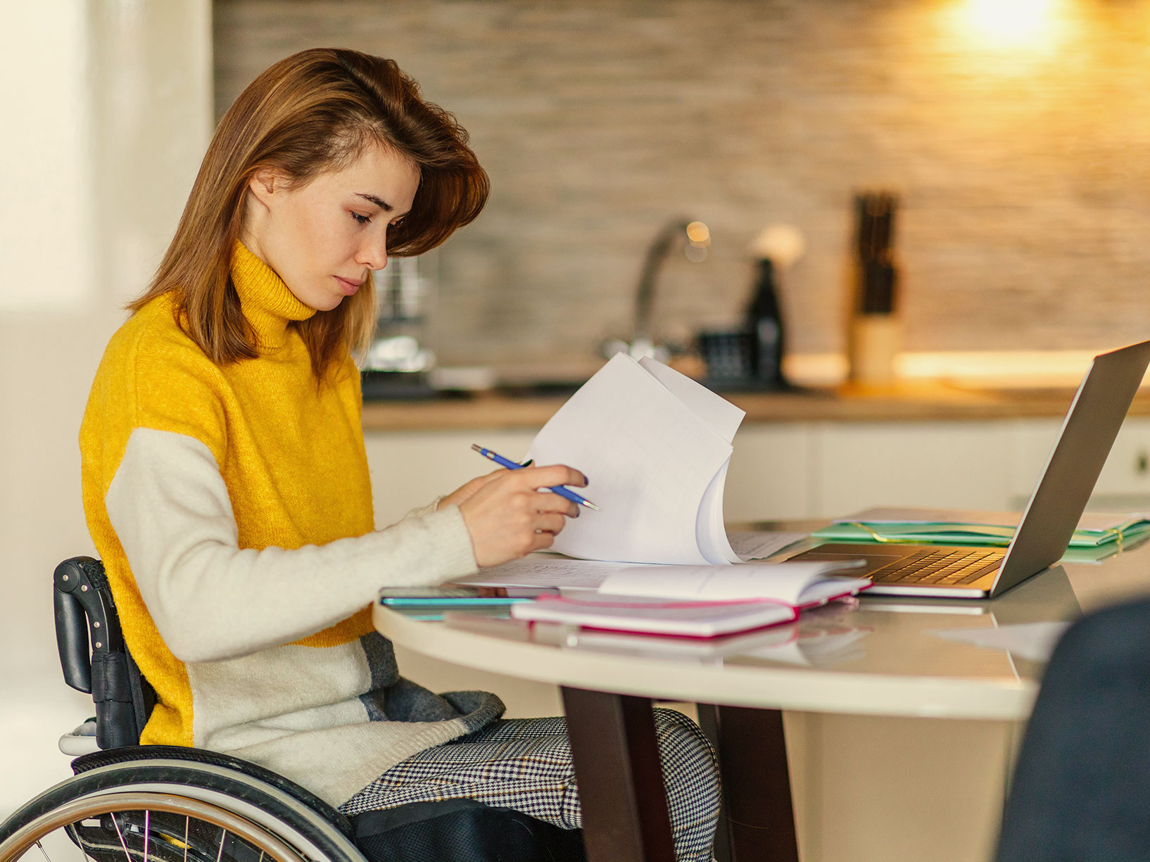 A woman in a wheelchair takes notes in front of a laptop.