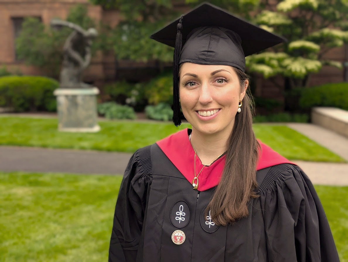 Becca Cable, 2025 ALM Grad standing in the grass in front of bronze replica of Myron's Discobolus statue.